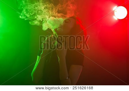 Young Woman In Neon Light And Smoke Of E-cigarettes Or Vape On Dark Background.