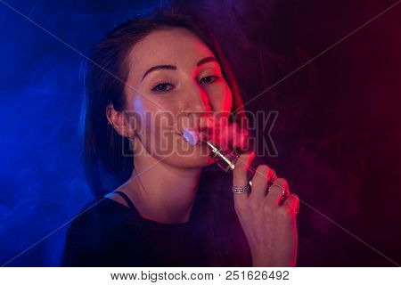 Portrait Of Asian Woman Smoking Vape Or E-cigarette In Neon Light At Black Background