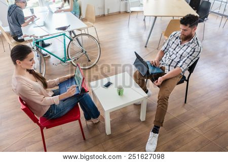 Dedicated young woman editing a document on laptop, while sharing the desk with other hard-working co-workers in a modern office space for digital nomads