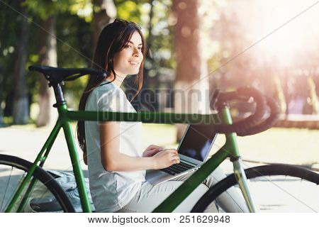 Pretty Girl With Green Bicycle Sitting On Beanch And Working With Laptop In The Sunny Summer Park, S