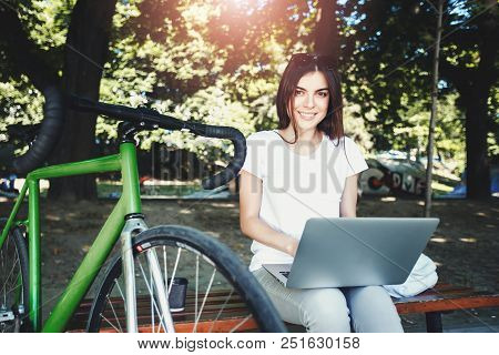 Cute Romantic Girl With Green Bicycle Sitting On Beanch And Working With Laptop In The Sunny Summer 
