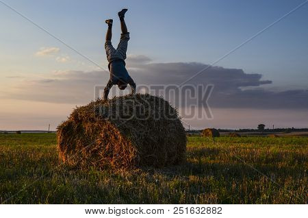 The Guy Makes A Stand On His Hands On A Roll Of Hay. Yoga In Nature