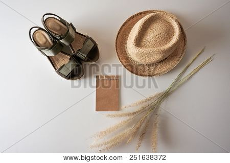Flat Lay Of Summet Hat, Khaki Sandals, Brown Note Pad And Dry Grass