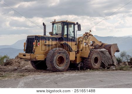 Excavator Single-bucket  For Harvesting Falling Stones On The Roadway In The Mountains, Is Parked At