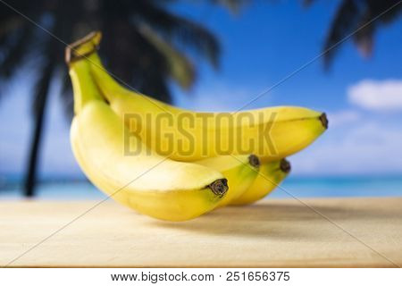 Group Of Five Whole Fresh Yellow Banana One Cluster With Palm Trees On The Beach In Background