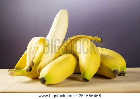 Lot Of Whole Fresh Yellow Banana And One Opened With Grey Gradient Behind