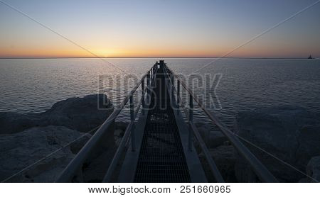 A Metal Gang Plank Juts Out Into The Water At Sunrise