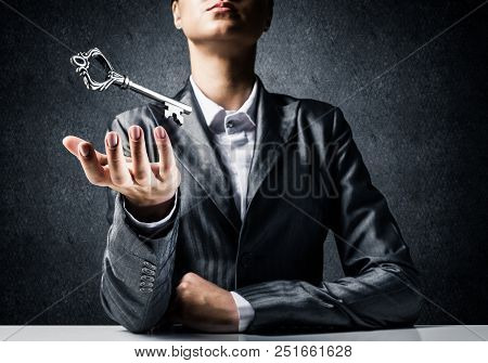 Cropped Image Of Businessman In Suit Keeping Big Key In Hand With Dark Wall On Background.