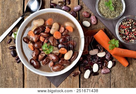 Close-up Of Full Bowl Of Hot Bean Soup With Large Beans On Cutting Board, Carrots, Parsley, Marjoram