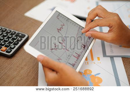 Closeup Of Trader Working With Candlestick Chart And Using Tablet. Papers And Calculator Lying On De