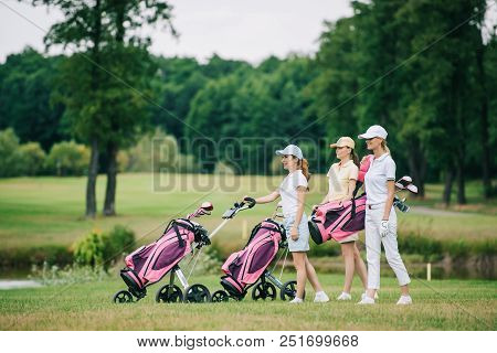 Side View Of Female Golf Players In Caps With Golf Equipment On Golf Course