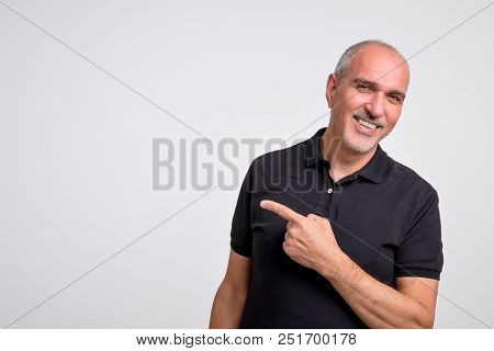 Mature Hispanic Man Pointing Aside Copy Space. Handsome Elder Man In Black Shirt Looking At Camera A