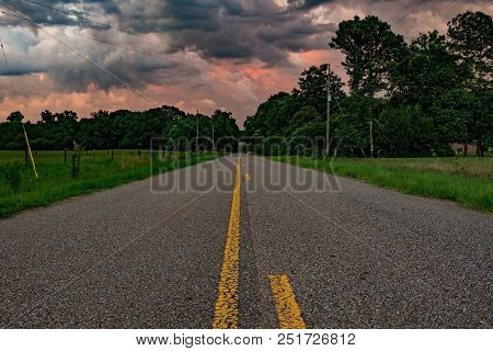 Paved Country Road Leading Toward A Firey Sunset Sky With A Low Point Of View