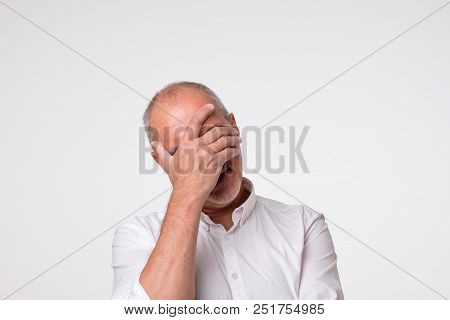 Displeased Mature Man In White Shirt Covering His Eyes Over Gray Background