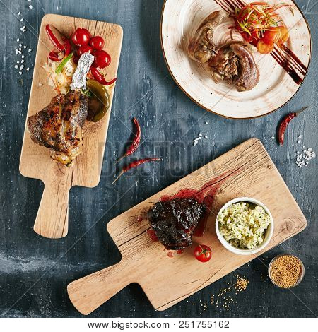 Set of Restaurant Main Course with Grilled Beef Cheeks, Lamb Leg and Tongues on Luxury Black Stone Top View. Various Meat Dishes Collection with Spices and Vegetables Flat Lay