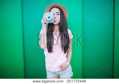 Beautiful Brunette Srtands And Poses On Camera. She Covers One Eye With Blue Camera. Girl Holds Heer