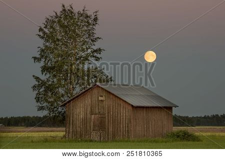 Barn In Farmfield By Tree With A Full Moon.