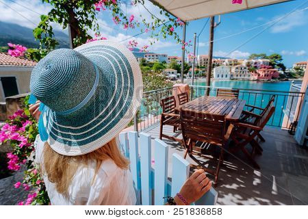 Assos Village, Kefalonia, Greece. Female Tourist In Blue Sunhat In Front Of Cozy Veranda Terrace Doo