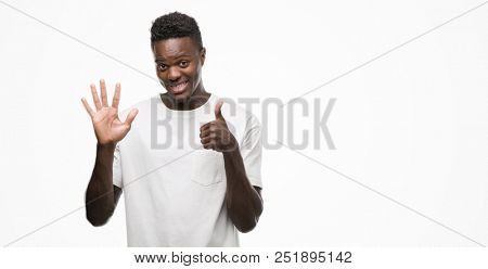 Young african american man wearing white t-shirt showing and pointing up with fingers number six while smiling confident and happy.