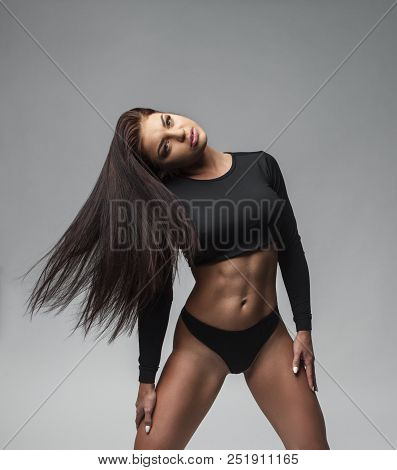 Attractive Sporty Woman In Black Bikini Posing On Grey Background. Photo Of Brunette Woman With Slim