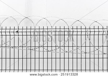 Fence With Barbed Wire On White Wall Background.