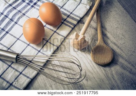 A Kitchen Setting With 2 Eggs, Towel, Wooden Spoon And Querl And An Eggbeater On A Table