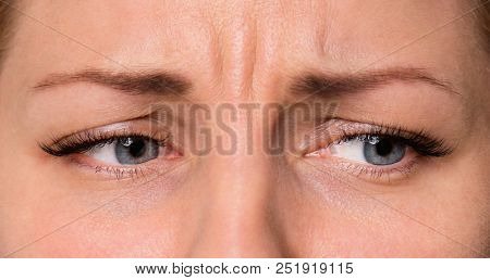 Close-up sad or unhappy face of beautiful young woman with beautiful grey eyes and big pretty eyelashes and eyebrows. Macro of human eyes looking away.