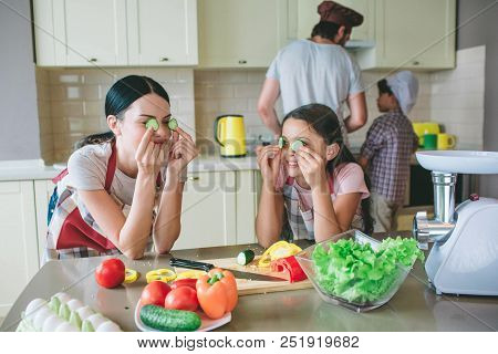 Moom And Daughter Stands Together And Leans At Table. They Are Playing With Round Pieces Of Cucumber
