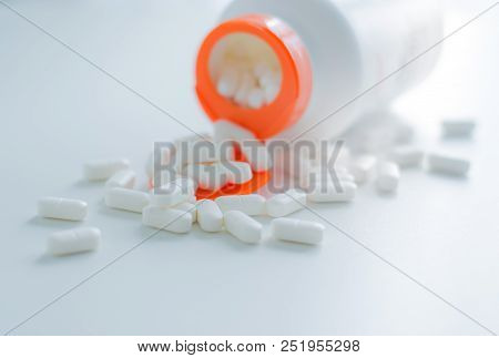 White Tablets Spilling Out Of Plastic White Bottle With A Tablet