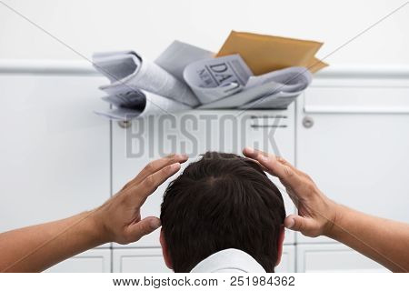 Close-up Of Man With Hand On Head In Front Of Overloaded Mailbox With Junk Mail
