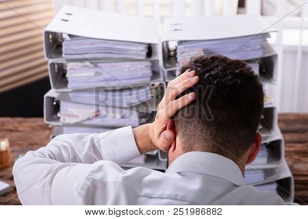 Close-up Of Stressed Businessman With Hand On Head In Front Of Stacked Folders