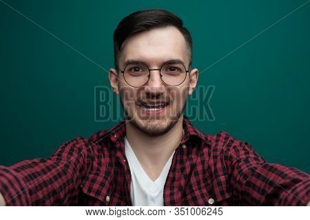Portrait Of A Chherful Young Man In Glasses Posing Against A Green Background.
