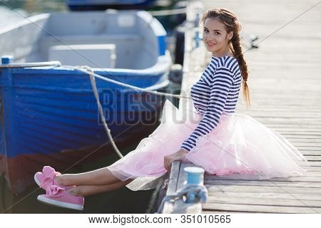 Happy Young Womanl With A Long Braid Happy Laughing While Sitting Outdoor With Boats On Background. 