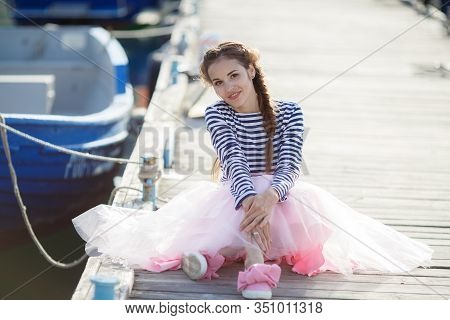 Happy Young Womanl With A Long Braid Happy Laughing While Sitting Outdoor With Boats On Background. 