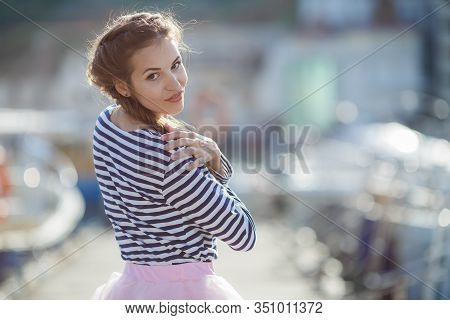 Happy Young Womanl With A Long Braid Happy Laughing While Sitting Outdoor With Boats On Background. 
