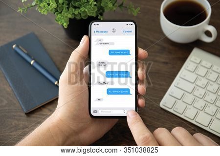 Male Hand Holding Phone With App Messenger On The Screen Over Table In The Office