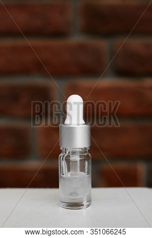 Bottle Of Serum, Hyaluronic Acid, Botulin On White Wooden Table. Grunge Red Brick Wall For Your Logo