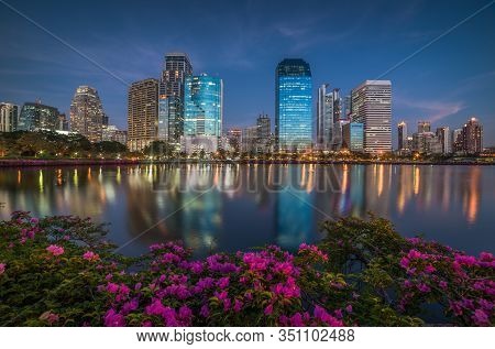 Lake With Purple Flowers In City Park Under Skyscrapers At Twilight. Benjakiti Park In Bangkok, Thai