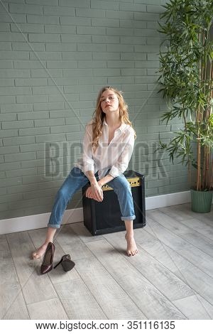 Young Beautiful Woman Sitting On Subwoofer With Bare Feet Next To Green Plant