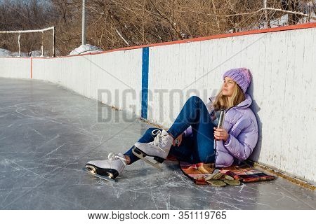 Lovely Young Woman Relaxing After Riding Ice Skates And Drinking Hot Drink From Termo Pot On The Ice