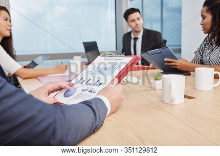 Business Team Gathered At Big Table To Discuss Charts And Digrams With Financial Data At Meeting
