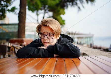 Teen Blond With Glasses Dressed In Black Sitting At A Table In The Outdoor Cafe