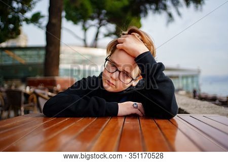 Teen Blond With Glasses Dressed In Black Sitting At A Table In The Outdoor Cafe