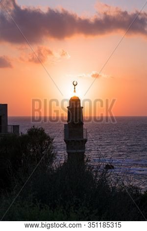 The setting sun plunges into the Mediterranean Sea. Round tower crowned with a crescent is a Muslim minaret. Old Yaffo, Tel Aviv. Concept active, informative and photo of tourism