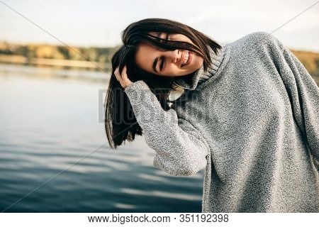 Smiling Happy Young Brunette Woman With Closed Eyes With Blowing Hair, Wearing Grey Sweater, Posing 