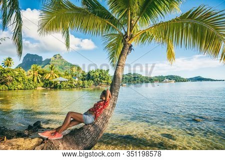 Tropical travel nature background tourist woman on eco tourism destination relaxing lying down on palm tree tropical landscape. Bora Bora island with Otemanu mountain view, Tahiti, French Polynesia.