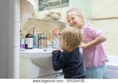 Two Cute Adorable Blond Caucasian Siblings Washing Face And Cleaning Tooth With Toothbrush At Bathro