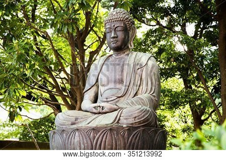 Photograph Of A Stone Buddha Statue With Trees In The Background