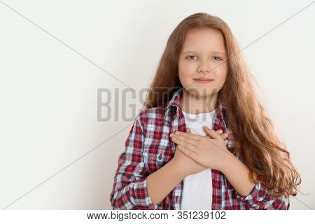 Cute Grateful Little Girl With Hands On Chest Against Light Background