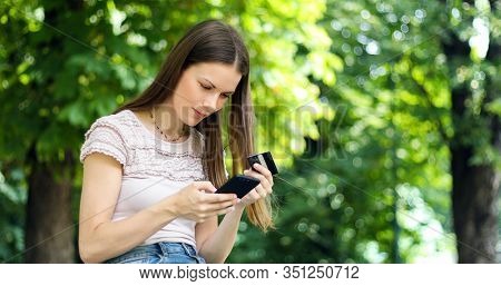 SPortrait of a happy woman paying online with credit card and smart phone in a park